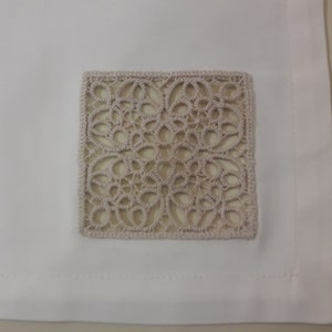 May include: White tablecloth with a beige square lace overlay in the centre.