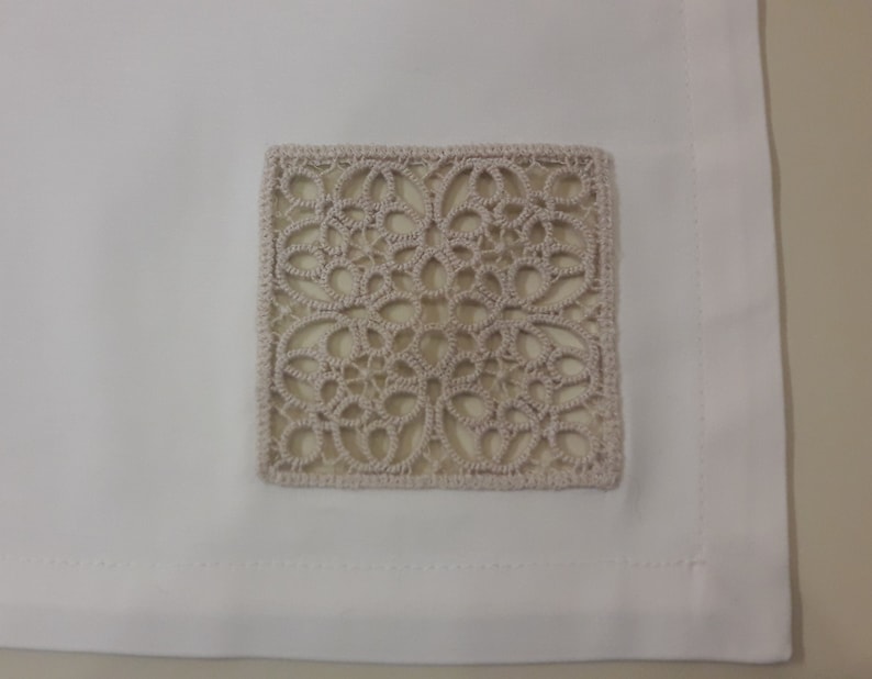 May include: White tablecloth with a beige square lace overlay in the centre.