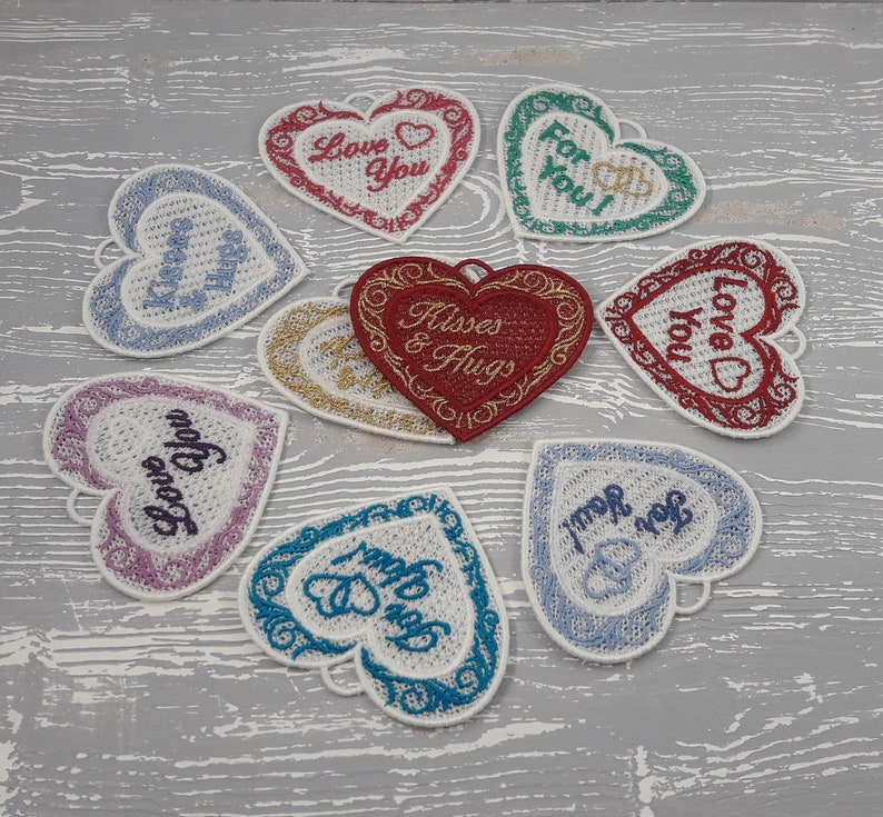 Pode incluir: Nove cora&ccedil;&otilde;es de feltro bordados com diferentes mensagens, incluindo "Love You", "Kisses & Hugs" e "For You!" Os cora&ccedil;&otilde;es est&atilde;o dispostos em c&iacute;rculo sobre uma superf&iacute;cie de madeira cinza.
