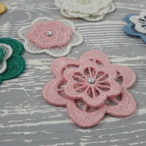 May include: Assortment of layered fabric flower embellishments with pearl and rhinestone accents. The flowers are in shades of pink, green, blue, white, and yellow.