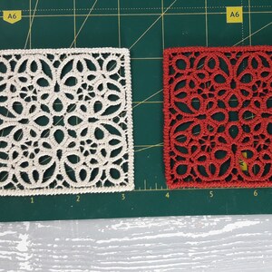 May include: Two square pieces of lace fabric, one white and one red, on a green cutting mat. The lace is a delicate pattern of circles and loops.