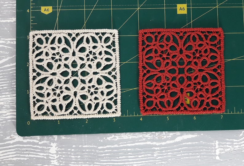 May include: Two square pieces of lace fabric, one white and one red, on a green cutting mat. The lace is a delicate pattern of circles and loops.