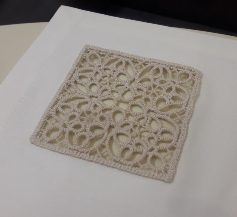 May include: A square piece of beige crochet lace with a delicate floral pattern.