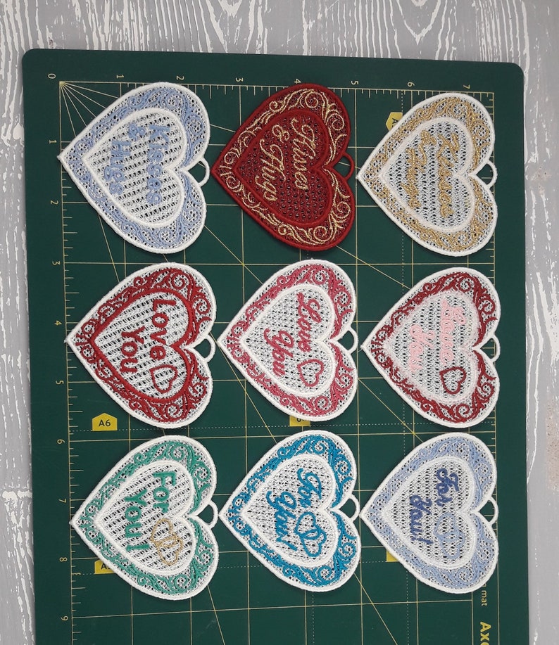 Pode incluir: Nove ornamentos brancos em forma de cora&ccedil;&atilde;o com desenhos e texto bordados. O texto nos ornamentos inclui "Love You", "Forever & Always", "For You", "Love You", "Love You", "For You", "For You", "For You" e "For You".