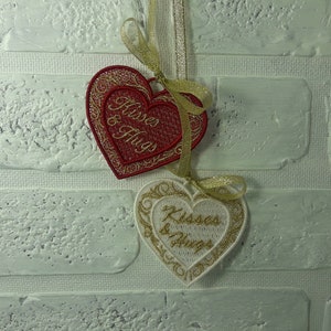 Pode incluir: Dois ornamentos bordados em forma de cora&ccedil;&atilde;o com fio dourado e o texto "Kisses & Hugs" em branco e vermelho.