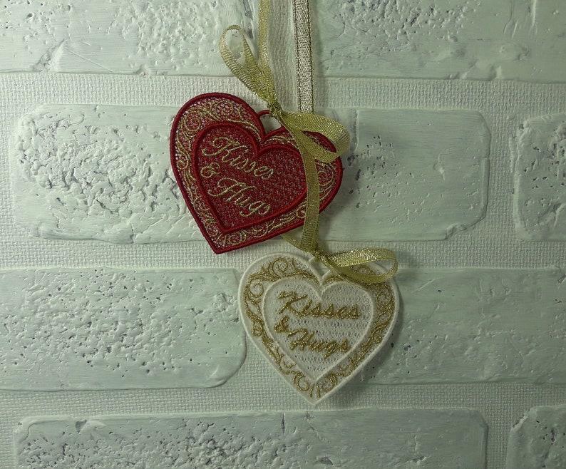 Pode incluir: Dois ornamentos bordados em forma de cora&ccedil;&atilde;o com fio dourado e o texto "Kisses & Hugs" em branco e vermelho.
