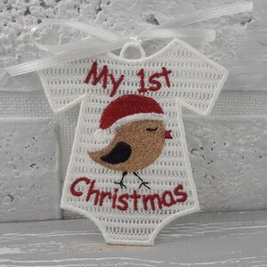 Pu&ograve; includere: Ciondolo a forma di body per neonato in crochet bianco con ricami rossi e marroni. Il body ha il testo "My 1st Christmas".