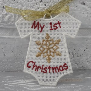 Pu&ograve; includere: Ciondolo a forma di body per neonato in crochet bianco con ricamo rosso che recita "Il mio primo Natale" e un design a fiocco di neve dorato.