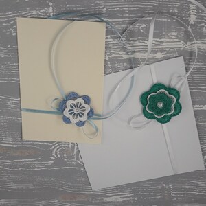 May include: Two white cards with blue and green ribbon tied around them. The ribbon is tied in a bow with a blue and white flower on one card and a green flower on the other.