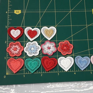 May include: Assortment of 10 embroidered patches in various colors and designs, including hearts, flowers, and lace. The patches are arranged on a green cutting mat.