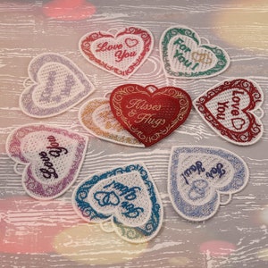 Pode incluir: Oito enfeites de cora&ccedil;&atilde;o de feltro bordados com diferentes mensagens sobre o amor, incluindo "Love You", "Kisses & Hugs" e "For You!" Os cora&ccedil;&otilde;es s&atilde;o de v&aacute;rias cores, incluindo vermelho, rosa, azul e verde.
