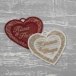 Pode incluir: Dois ornamentos bordados em forma de cora&ccedil;&atilde;o com fio dourado. O cora&ccedil;&atilde;o vermelho tem o texto "Kisses & Hugs" em fio dourado. O cora&ccedil;&atilde;o branco tem o texto "Kisses & Hugs" em fio dourado.