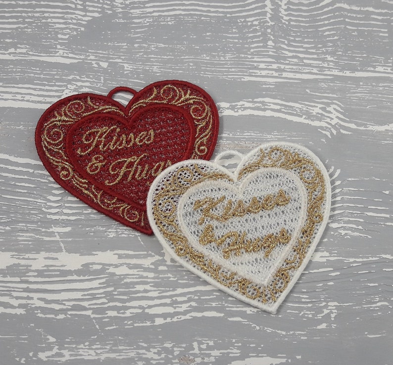 Pode incluir: Dois ornamentos bordados em forma de cora&ccedil;&atilde;o com fio dourado. O cora&ccedil;&atilde;o vermelho tem o texto "Kisses & Hugs" em fio dourado. O cora&ccedil;&atilde;o branco tem o texto "Kisses & Hugs" em fio dourado.