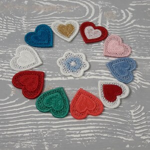 May include: A collection of ten embroidered fabric hearts in various colors, including red, pink, blue, green, and white. The hearts are arranged in a circle on a white wooden surface.
