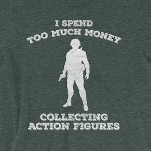 May include: A dark green t-shirt with a white silhouette of a person holding a gun and the text "I spend too much money collecting action figures".