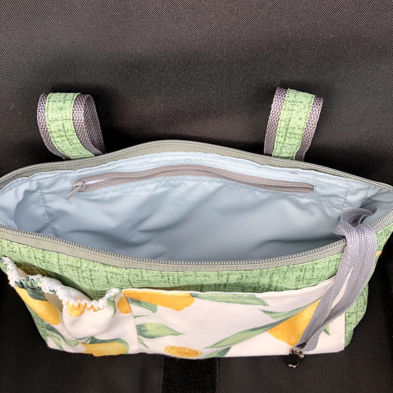 Op de afbeelding: Een groene stoffen tas met een citroenprint op het voorvak en een lichtblauwe voering. De tas is voorzien van een ritssluiting aan de bovenkant, twee groene stoffen hengsels aan de bovenzijde en een extra ritsvak in het hoofdvak.