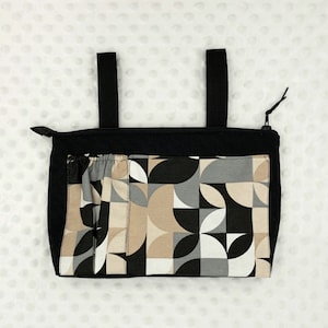 Könnte beinhalten: Schwarze Tragetasche mit Reißverschluss und zwei Henkeln. Die Tasche hat ein geometrisches Muster in Braun-, Schwarz-, Weiß- und Grautönen.