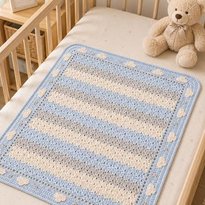 May include: A rectangular crochet baby blanket featuring alternating horizontal stripes in light blue, cream, and grey. The blanket is finished with a light blue border decorated with small, evenly spaced cream-coloured crochet cloud motifs.