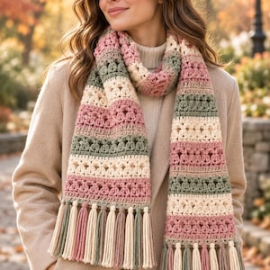 May include: A long, crocheted scarf featuring horizontal stripes in muted shades of sage green, dusty rose, and cream. The scarf displays a repeating textured stitch pattern and is finished with long, multi-coloured fringe tassels at both ends.
