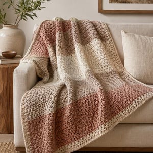 Könnte beinhalten: Eine rechteckige Häkeldecke mit einem Color-Block-Muster aus terrakottafarbenem, beigem und cremefarbenem Garn. Das Textil weist durchgehend ein gleichmäßiges Strukturmuster auf, mit breiten horizontalen Streifen in einer wiederkehrenden Abfolge.
