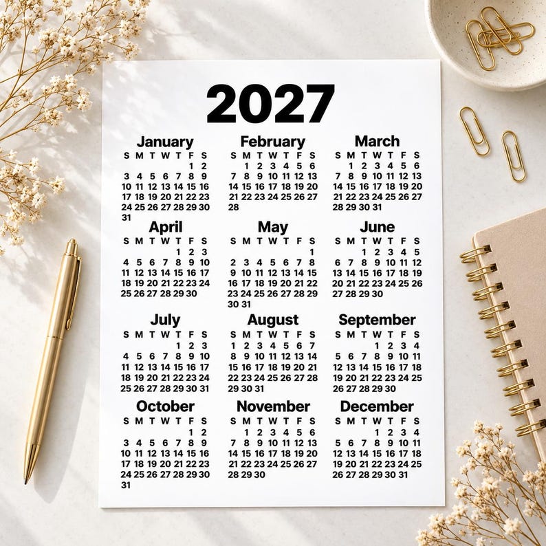 Minimalist 2027 printable calendar shown as a flat lay on a light desk surface, styled with dried flowers, a gold pen, paper clips, ceramic dish and spiral notebook for an elegant stationery-themed mockup.