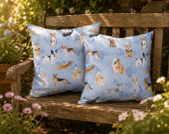 Peut inclure: Deux coussins carrés avec un motif bleu clair représentant différentes races de chiens. Les coussins sont posés sur un banc en bois, entourés de fleurs et de verdure dans un cadre de jardin.