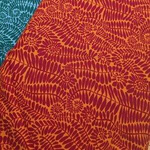 May include: Close-up of two fabrics with floral patterns. One fabric is orange with a red floral design. The other fabric is teal with a white floral design. The fabrics are folded over each other.