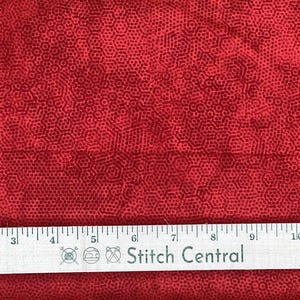 May include: Red fabric with a repeating pattern of small, dark red hexagons. A ruler with inch measurements and the text "Stitch Central" is at the bottom. The fabric is likely used for sewing or quilting projects.
