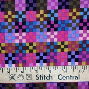 May include: A fabric featuring a repeating geometric grid pattern of small squares in shades of pink, purple, blue, yellow, and black. A wooden ruler is positioned at the bottom, showing measurements in inches from 4 to 11 inches.