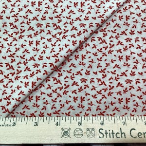May include: White fabric with a red leaf print. The fabric is folded in half and a ruler is placed on top of the fabric. The ruler is marked with inches and the text "Made in U.S.A." is visible. The text "Stitch Central" is also visible on the ruler.