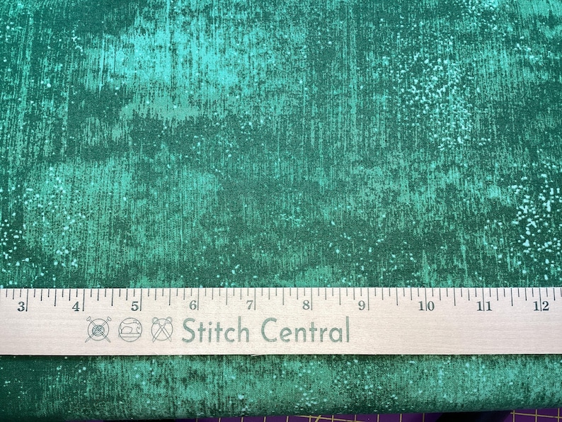 Może przedstawiać: Zbliżenie na tkaninę w kolorze turkusowym z fakturą w kropki. Na tkaninie leży drewniana linijka z napisem "Stitch Central".