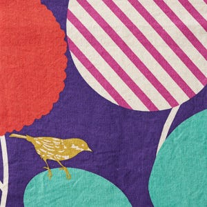 May include: A fabric textile featuring a deep purple background with a repeating pattern of large circular shapes. One circle has magenta and white diagonal stripes, while others are solid red or teal. A small yellow bird is perched on a teal circle.