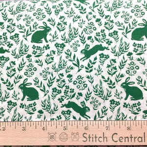 May include: White fabric with a repeating pattern of green rabbits and foliage. The design includes various poses of rabbits among stylized leaves and flowers. A wooden ruler with inch markings is at the bottom.