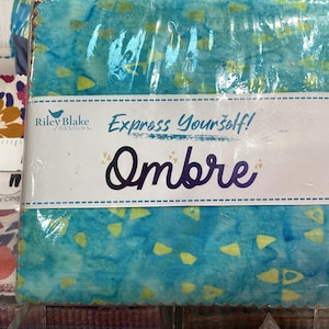 May include: A blue and yellow fabric with a white label that says "Riley Blake Designs" and "Express Yourself! Ombre".