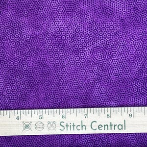 May include: Close-up of a purple fabric with a repeating pattern of small, interconnected circles. The fabric has a textured appearance and a ruler with the text "Stitch Central" is at the bottom.