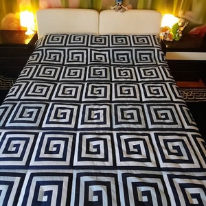 May include: A white bed with a blue and white patterned duvet cover. The duvet cover has a geometric pattern of squares with a Greek key design.