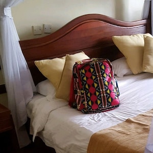 May include: A white canopy bed with a wooden headboard and a patterned backpack on the bed. The bed has a white sheet and a brown blanket. There is a rug on the floor.