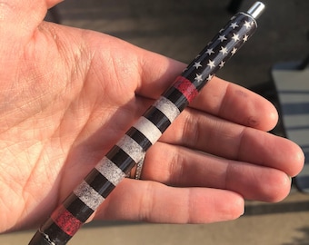 May include: A decorative pen with a patriotic design. The pen features a black barrel with alternating sections of white and black stripes, red stripes, and a section with white stars on a black background. The pen has a silver tip and a black ink cartridge.