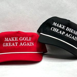May include: Two baseball caps, one red and one black, with white text. The red cap says "MAKE GOLF GREAT AGAIN" and the black cap says "MAKE DIESEL CHEAP AGAIN". Both have a white rope detail.