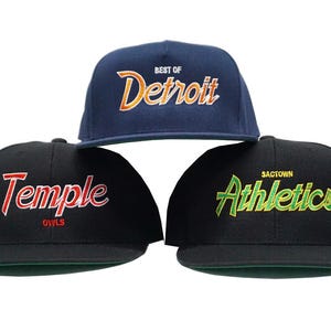 Może przedstawiać: Trzy czarne czapki bejsbolowe z różnymi haftowanymi logo. Pierwsza czapka ma napis "Best of Detroit" w pomarańczowych i żółtych literach. Druga czapka ma napis "Temple Owls" w czerwonych literach. Trzecia czapka ma napis "Sactown Athletics" w zielonych literach.