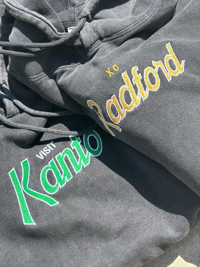 May include: Black hooded sweatshirt with green and white embroidery that says "VISIT KANTO" and yellow embroidery that says "Radford" with the letters "XC" above it.