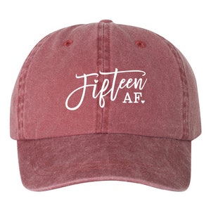May include: A maroon baseball cap with the text "Fifteen AF" in white script. The cap has a curved brim and a classic six-panel design, suitable for casual wear.