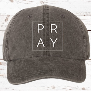 May include: A dark gray baseball cap with a white square on the front that says "PRAY" in all caps.
