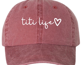 May include: A red, distressed, baseball cap with the text "titi life" and a white heart embroidered on the front.