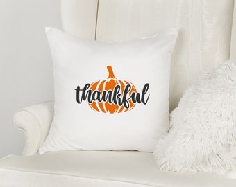 May include: White throw pillow with a black and orange pumpkin design and the word "thankful" in black script.