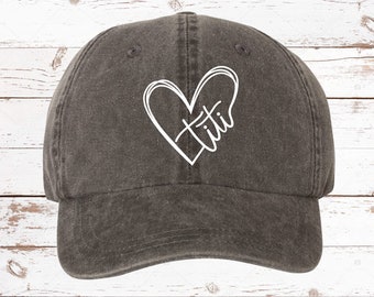 May include: A black denim baseball cap with a white heart design and the word "titi" inside the heart.