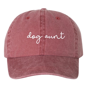 May include: A red, vintage-style baseball cap with the text "dog aunt" embroidered in white on the front.