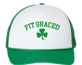 Puede incluir: Gorra de camionero verde y blanca con la inscripción "FIT SHACED" en verde y un trébol verde. La gorra tiene un panel frontal blanco, una visera verde y una parte trasera de malla verde.