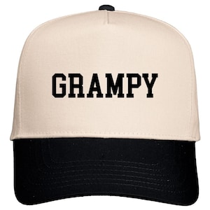 May include: A beige and black baseball cap with the word "GRAMPY" printed in black on the front.