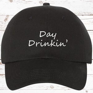 May include: Black baseball cap with white embroidered text that reads "Day Drinkin'"